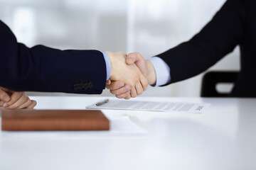 Business people shaking hands while sitting at the desk at meeting or negotiation, close-up. Group of unknown businessmen in a modern office. Teamwork, partnership and handshake concept