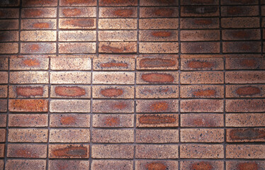 Old grunge light orange, brown and red brick wall background in lighting and high contrast at the light corner, bright in the middle.