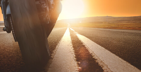 deep perspective of a motorcycle driving towards the sun on an empty road