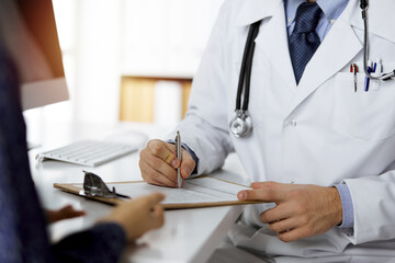 Friendly red-bearded doctor and patient woman discussing current health examination while sitting...