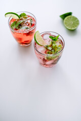 Raspberry cocktail, lemonade with lime, kiwi, mint and pieces of ice on a white table.