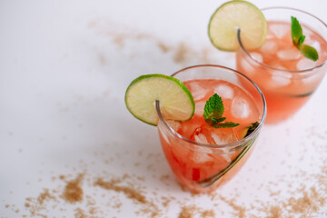 Grapefruit cocktail, lemonade with lime, mint and pieces of ice on a white table with cane sugar.