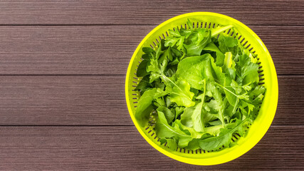 leaves of fresh lettuce, arugula, celery and parsley in a metal colander on the table top view. background with fresh greenery.