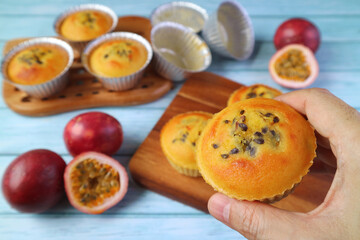 Naklejka na ściany i meble Closeup Fresh Baked Homemade Passion Fruit Muffins in Hand against Blurry Messy Kitchen Table