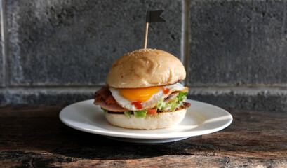 Home made tasty hamburger with bacon onion cheese lettuce and egg on white plate on wooden table.