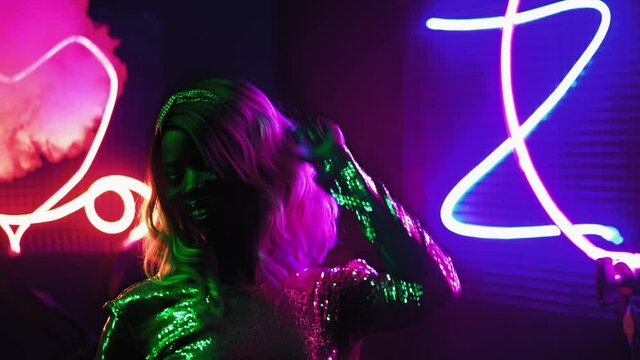 Happy African-American blondie girl with hair dances herself in neon lighting and machine smoke in a silver sequin dress on a black background. Neon concept. Prores 422.
