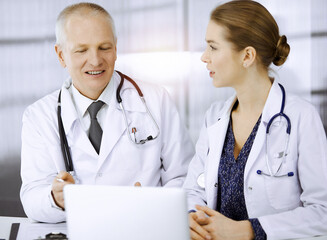 Elderly doctor and his female colleague discussing current disease therapy while sitting at working...