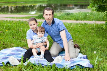 Single father and two daughters sitting on blanket on lawn in urban park, toddler kid and teenage girl, outdoor portrait