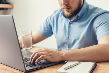 Business man in blue shirt working online, typing on laptop keyboard at the wooden table in the office, business, freelance or study concept