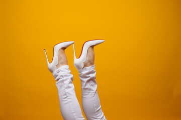 Female feet in beautiful white stiletto shoes, yellow background copy space.