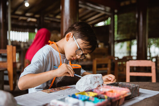 boy enthusiastically paints clay handicrafts with paint on pottery in the workshop gallery