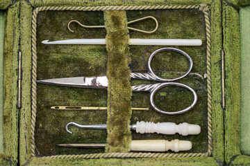 Top view of antique rare sewing kit in open green velvet box with scissor, sewing needles and crochet hooks made of metal and animal bones in very good condition