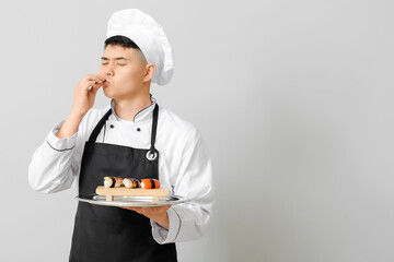Handsome Asian chef with sushi rolls on grey background