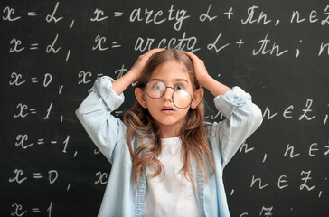 Stressed little schoolgirl near blackboard in classroom