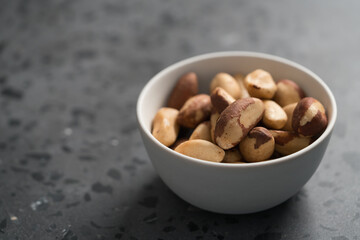 Brazil nuts in white bowl on concrete background with copy space