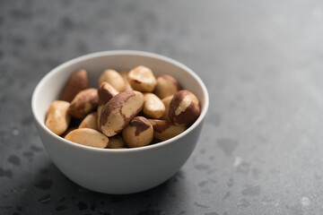 Brazil nuts in white bowl on concrete background with copy space