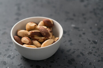 Brazil nuts in white bowl on concrete background with copy space