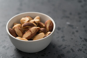 Brazil nuts in white bowl on concrete background with copy space