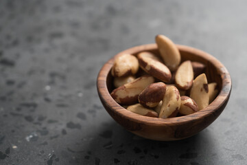 Brazil nuts in olive wood bowl on concrete background with copy space