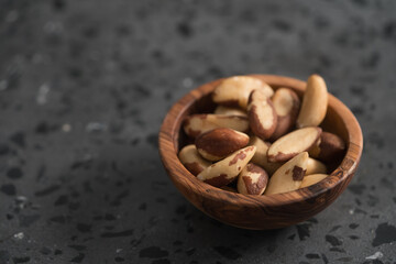 Brazil nuts in olive wood bowl on concrete background with copy space