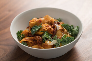fettuccine pasta with sun-dried tomatoes, almond flakes and kale leaves in white bowl on walnut table