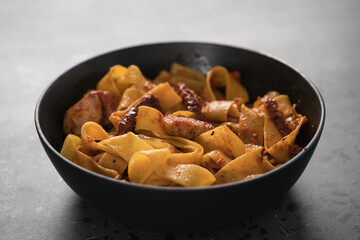 fettuccine pasta with fried chicken and sun-dried tomatoes in black bowl on concrete background