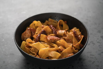 fettuccine pasta with fried chicken and sun-dried tomatoes in black bowl on concrete background