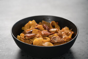 fettuccine pasta with fried chicken and sun-dried tomatoes in black bowl on concrete background
