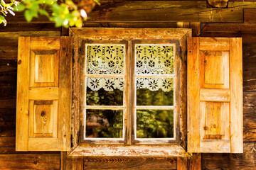 Wooden window with lace curtain and wooden shutters in an old wooden country house on a sunny day with no people. The building shows ancient type houses in Poland.