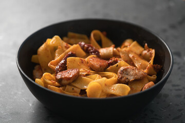 fettuccine pasta with fried chicken and sun-dried tomatoes in black bowl on concrete background
