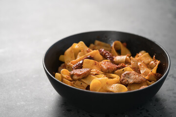 fettuccine pasta with fried chicken and sun-dried tomatoes in black bowl on concrete background