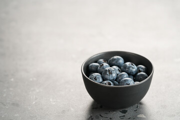 Ripe blueberries in black bowl on concrete background with copy space