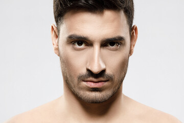 Obraz premium Headshot portrait of serious handsome guy standing with naked shoulders, concept of men beauty and power, isolated on gray background