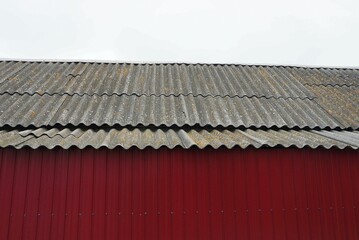 gray slate roof of a private house behind a red metal fence against the sky