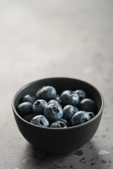 Ripe blueberries in black bowl on concrete background with copy space