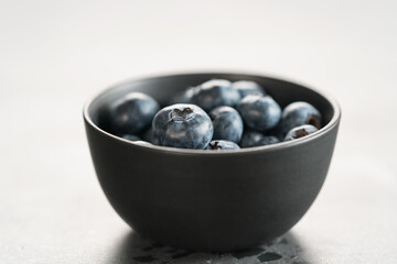 Ripe blueberries in black bowl on concrete background closeup