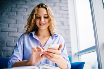 Emotional hipster girl rejoicing sms message on cellular sitting at book