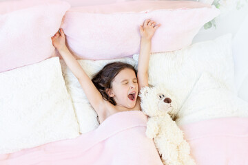 morning of a little girl 5-6 years old, a girl yawns in bed with a Teddy bear