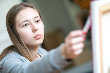 Concentrated young woman painting on canvas