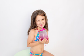 a little girl of 5-6 years old is sitting in a swimsuit with a cocktail on a white isolated...