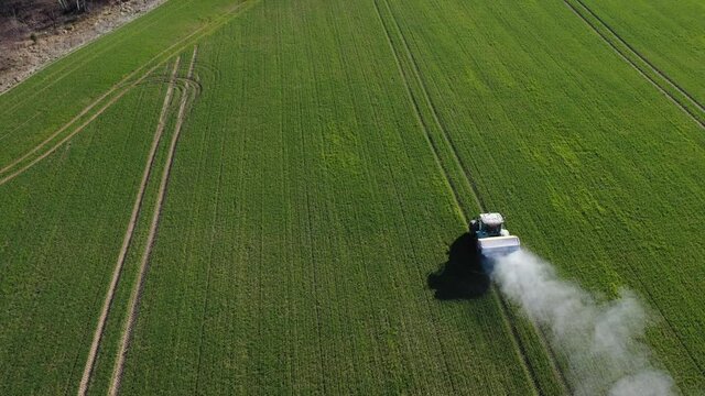 Tractor spreading fertilizers on spring crop field, aerial view


