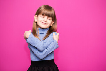 Cute little girl hugs herself, smiling carefree and happy.