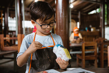 Boy painting crafts with colors in the pottery gallery along with friends