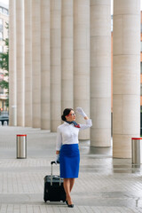 Stylish full length flight attendant in uniform with white gloves goes to work with a suitcase