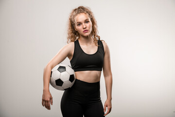 Pretty young female soccer player with long blond curly hair holding ball