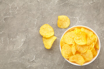 Potato chips on bowl on grey concrete background. Top view