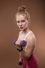 Young serious strong sportswoman holding dumbbells during exercise for arms