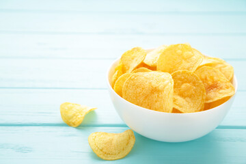 Potato chips on bowl on blue wooden background