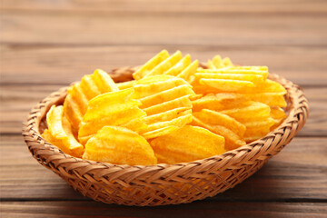 Potato chips in basket on brown wooden background.