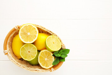 Organic lemons and limes in a basket on white wooden background with copy space